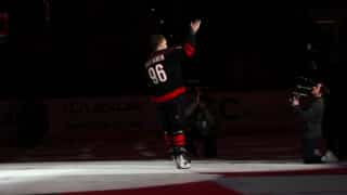 Mikko Rantanen kiittää yleisöä ensimmäisen Carolina Hurricanes -kotiottelunsa jälkeen. Hallissa on pimeää ja Rantanen on valokeilassa.