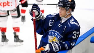 Atro Leppänen pelasi maajoukkueessa Leijonat-paidassa Sveitsin turnauksessa. Kuvassa mies valmistautuu otteluun alkulämmittelyssä ja nojailee kaukalon laitaa vasten.